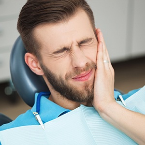 Man in dental chair holding cheek