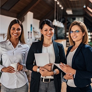 Three women are standing together holding papers and smiling.