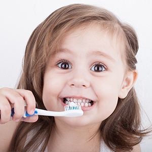 A little girl is holding a toothbrush in her mouth.