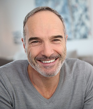 A man with grey hair and a gray shirt smiling.