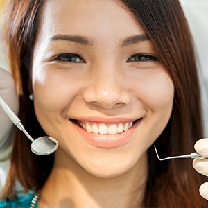 A woman with braces holding two dental instruments.