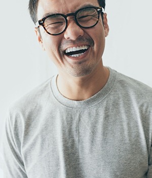 A man with glasses and a gray shirt is laughing.